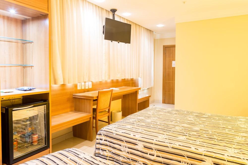 호텔 아틀란티코 비즈니스 센트로 리오데자네이루 외부 사진 The photo shows a hotel room with two beds featuring striped bedding. There is a wooden desk and chair near a window with light-colored curtains. A flat-screen television is mounted on the wall, and there appears to be a small refrigerator or mini-ba