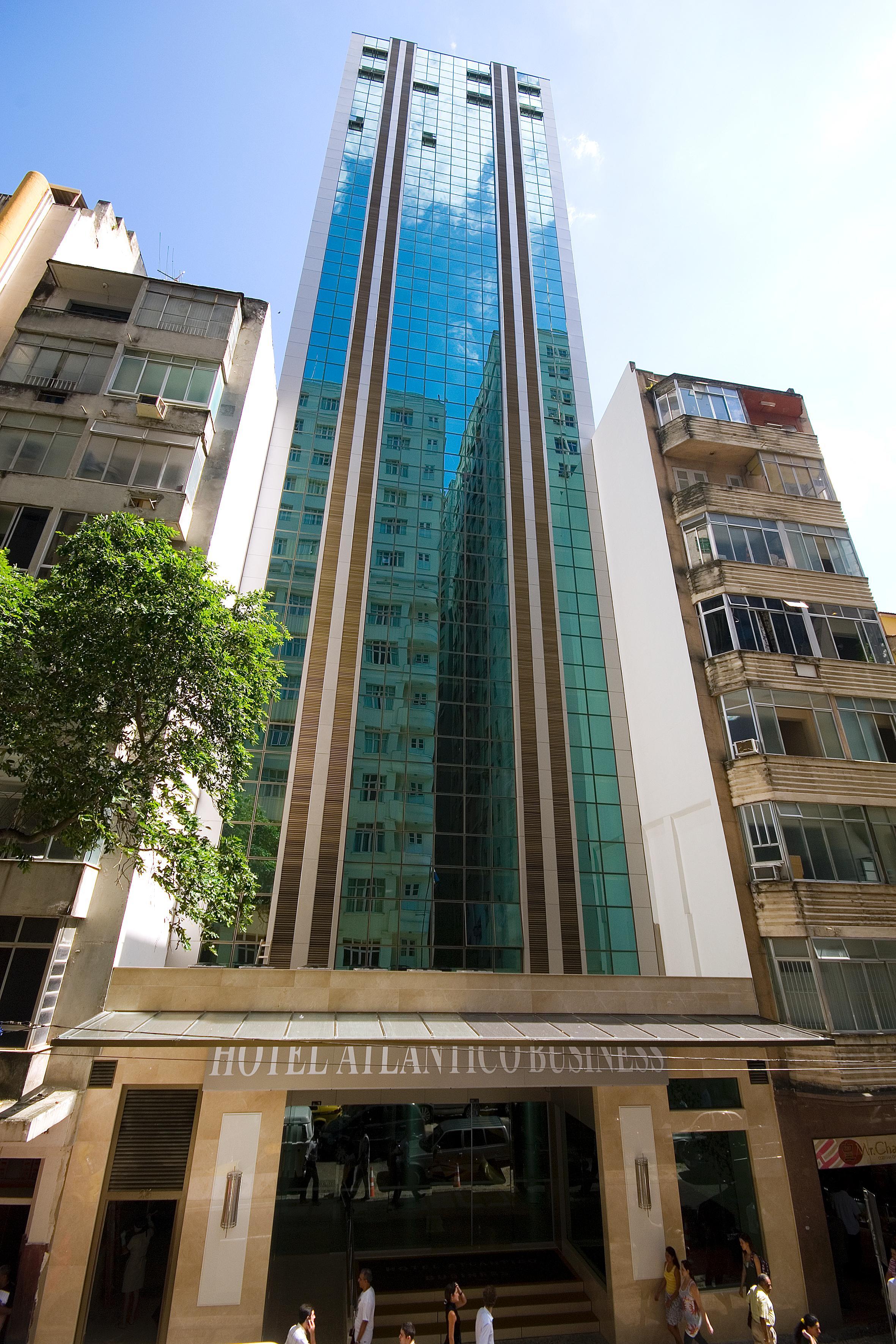 호텔 아틀란티코 비즈니스 센트로 리오데자네이루 외부 사진 The photo shows a modern multi-story building with a sleek glass facade. The building appears to have several floors with large windows, reflecting sunlight, and is flanked by a tree on one side and an older, more traditional residential structure on