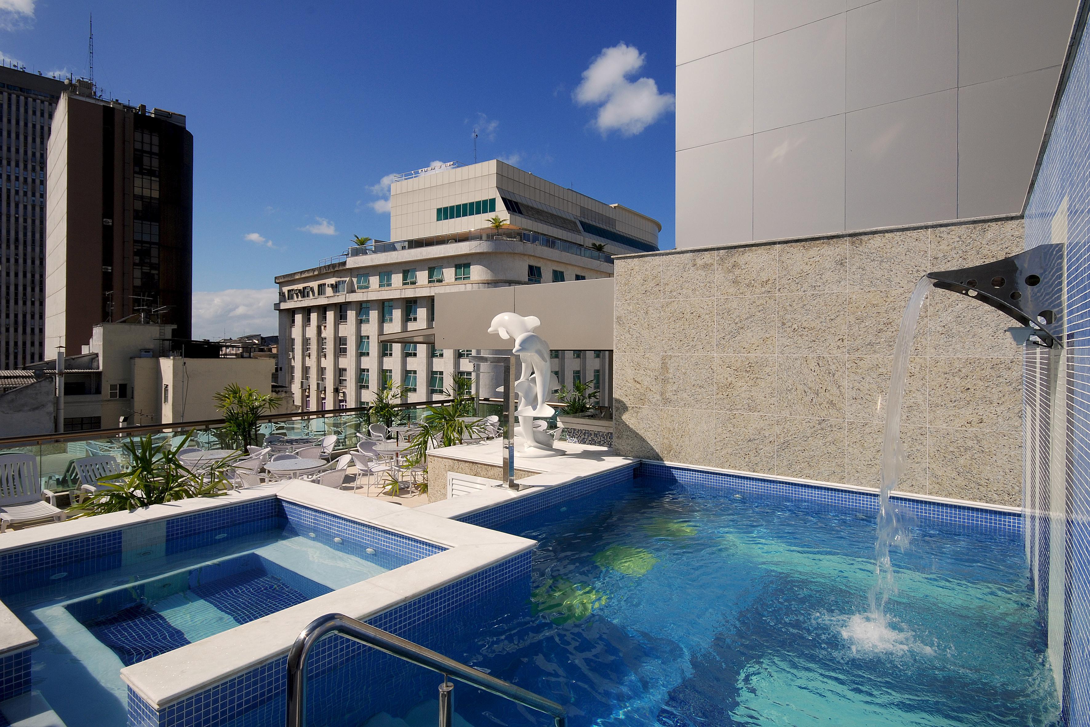 호텔 아틀란티코 비즈니스 센트로 리오데자네이루 외부 사진 The photo shows a rooftop area featuring a swimming pool and a spa. The pool is inviting with a clear blue water, and there appears to be a waterfall feature. Surrounding the pool are areas for relaxation, possibly with sun loungers. In the backgroun